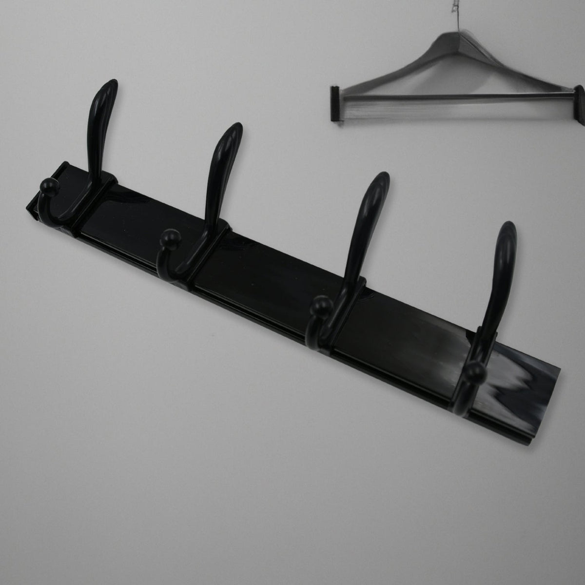 Black four-hook coat rack mounted on a light wall, with a dark wooden clothes hanger visible above it.
