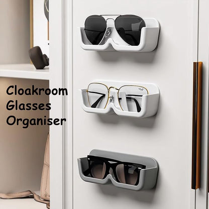 Three wall-mounted glasses holders, two white and one gray, holding different pairs of glasses on a white cabinet.