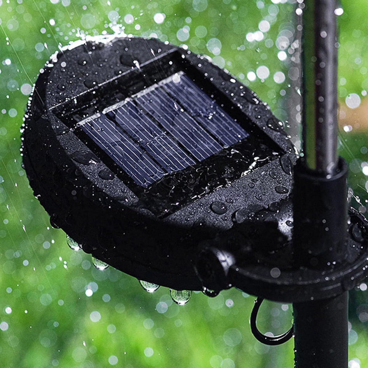 A close-up of a black solar panel on a garden light, covered in raindrops, against a green background.