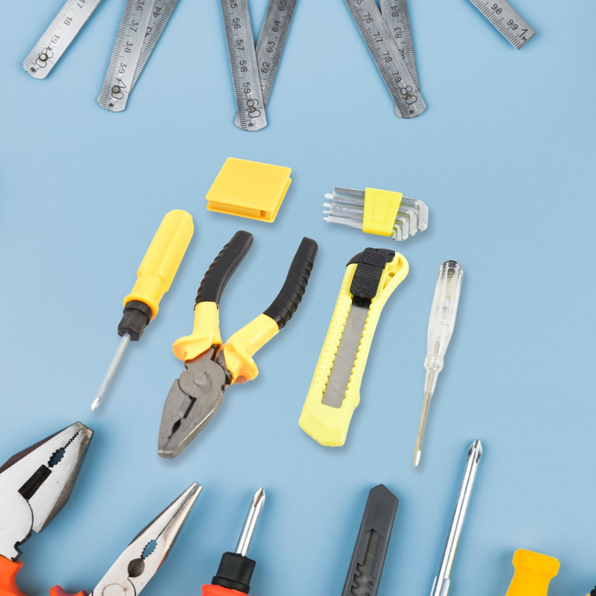 Various yellow and black tools, including screwdrivers, pliers, and a utility knife, scattered on a light blue surface with