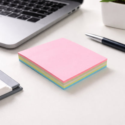 A stack of pink, yellow, and blue sticky notes on a white desk next to a laptop and a black pen.