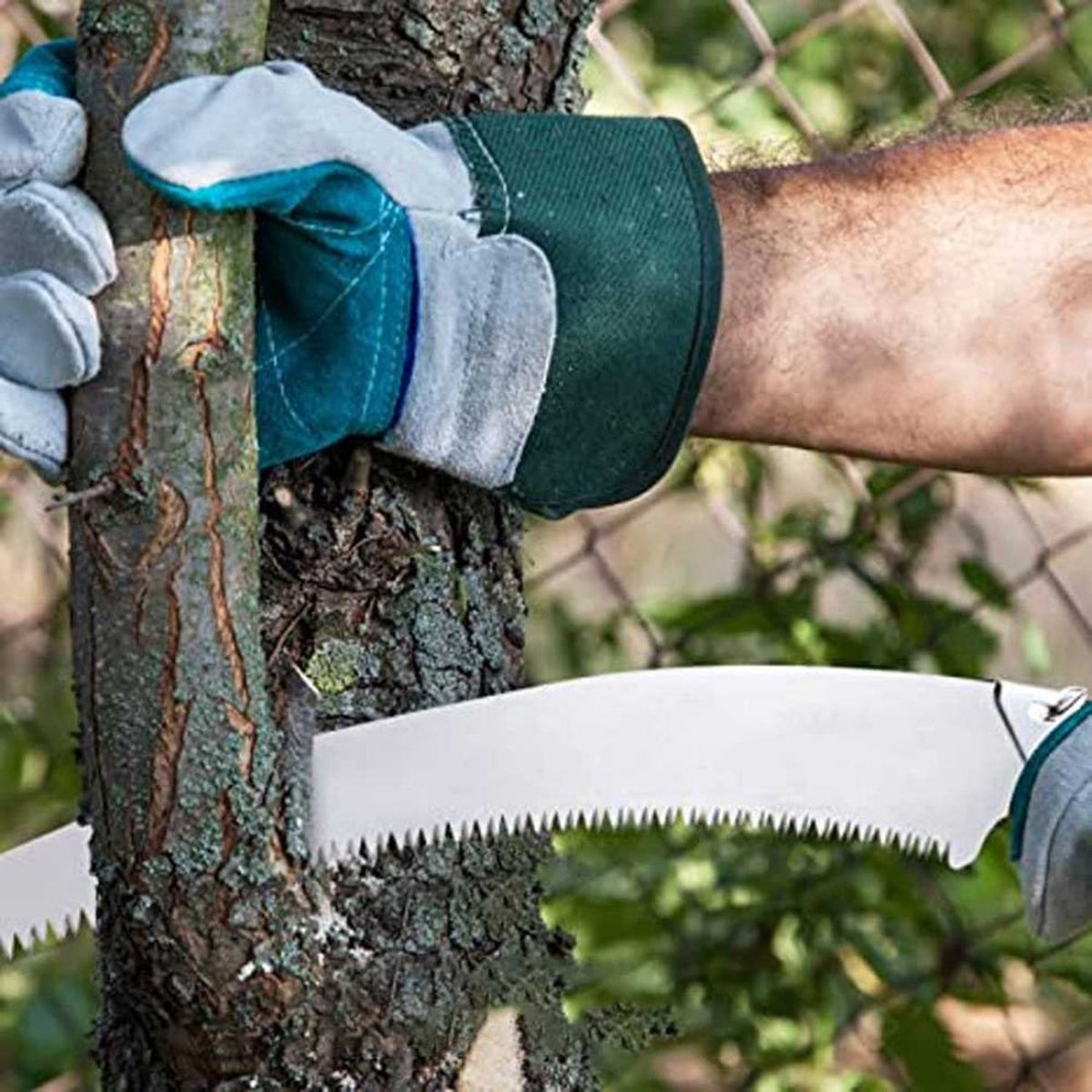 A gloved hand holds a tree trunk while a silver folding hand saw cuts into it.