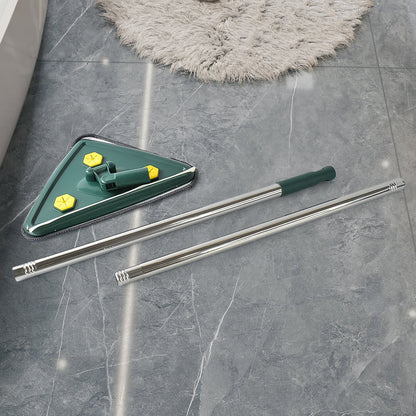 The green triangle mop head and its disassembled silver extendable handle lie on a dark gray tiled floor next to a fluffy