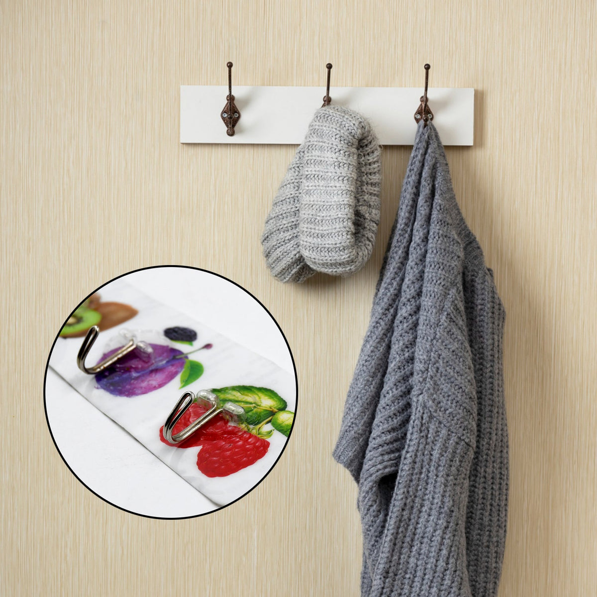 A close-up of the fruit-themed adhesive hooks is inset over a blurred image of a different, plain white coat rack with a hat