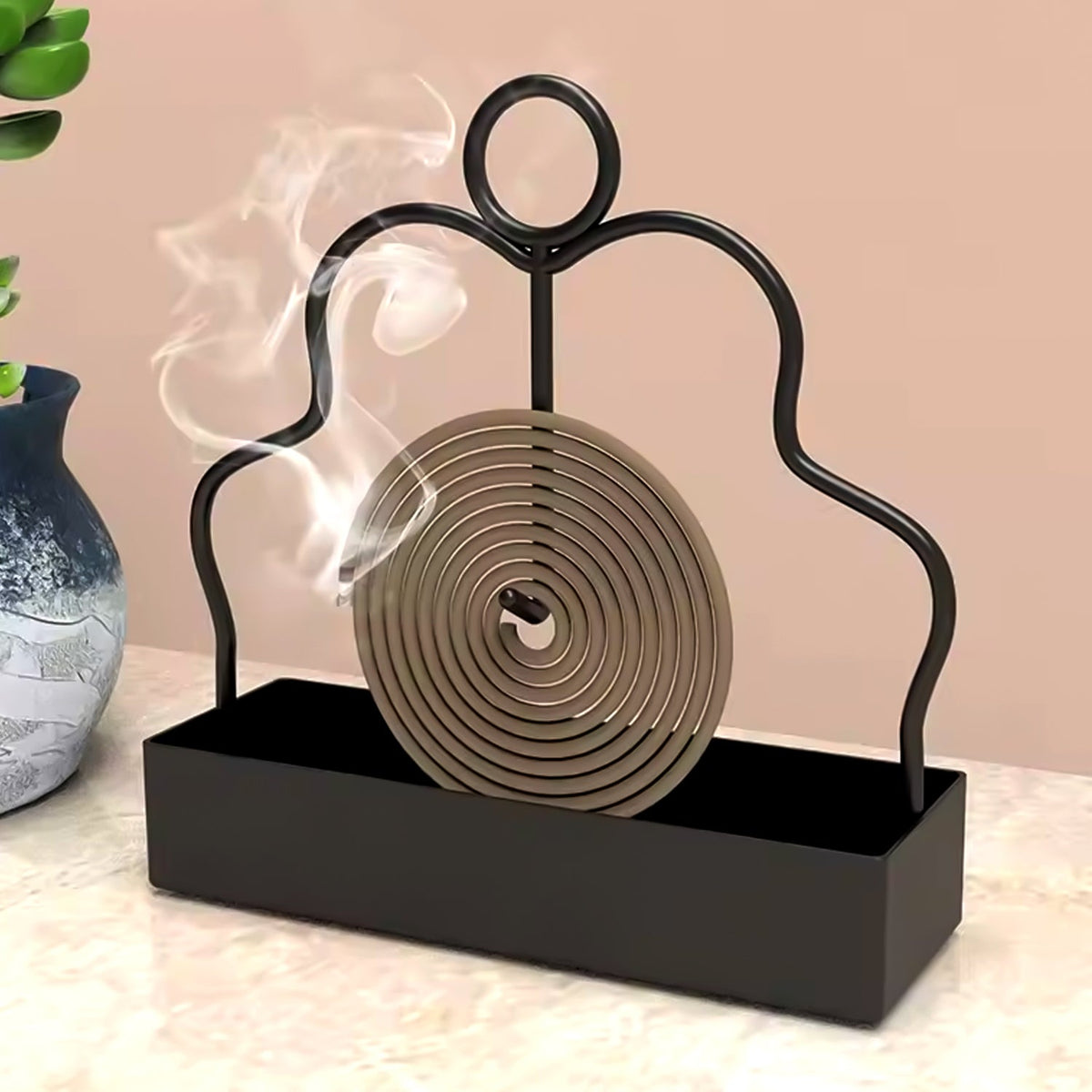 A black metal mosquito coil holder with a burning brown spiral coil emitting smoke next to a blue vase.
