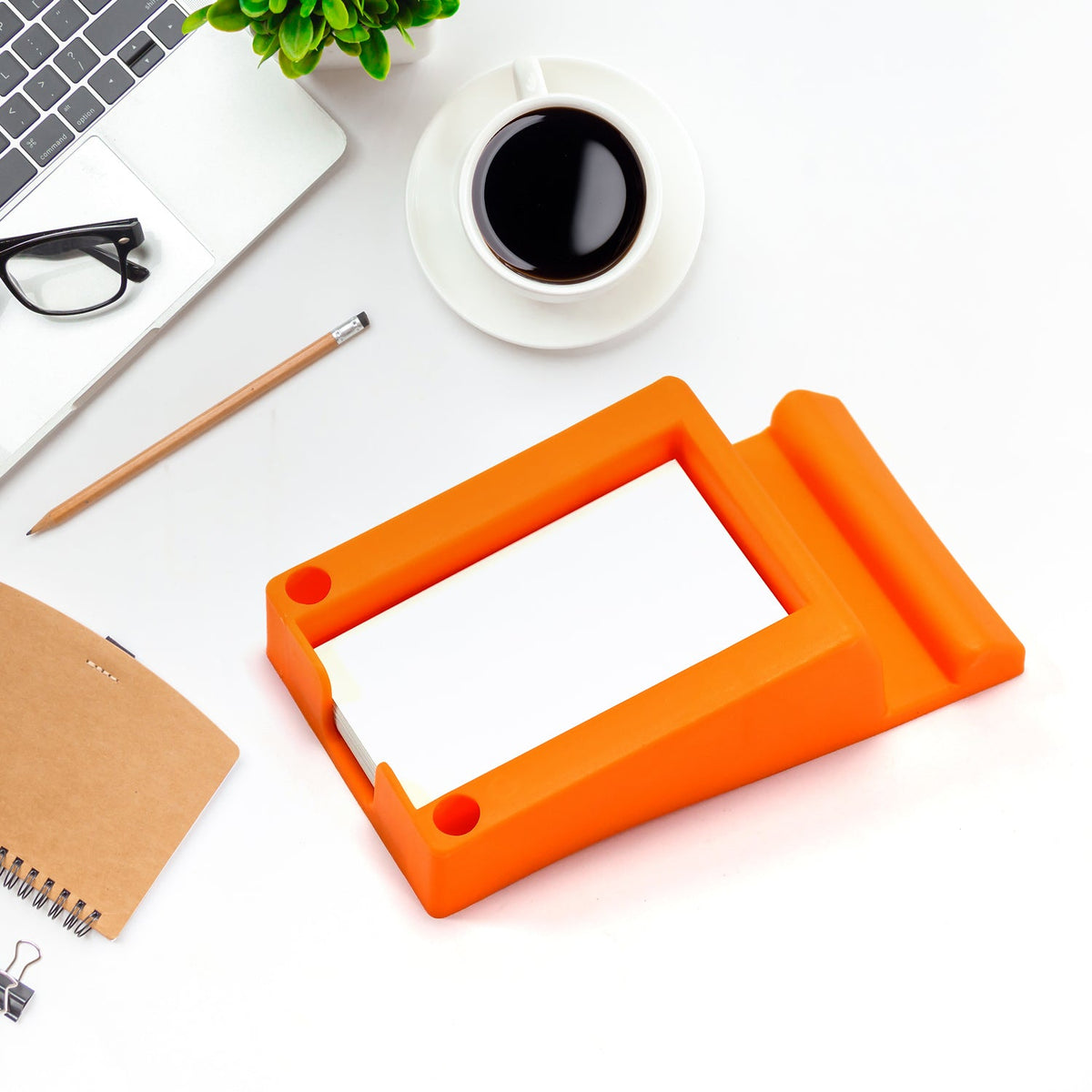 An orange plastic holder on a white desk, holding a stack of white business cards, with a laptop and coffee nearby.