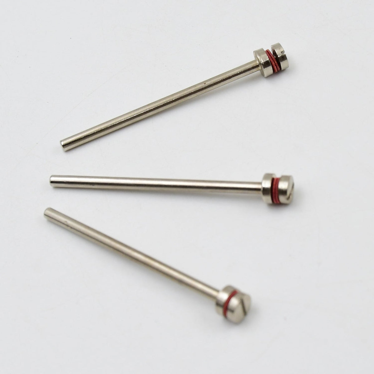 Three silver mandrels with red bands and screw heads lie scattered on a plain white background.
