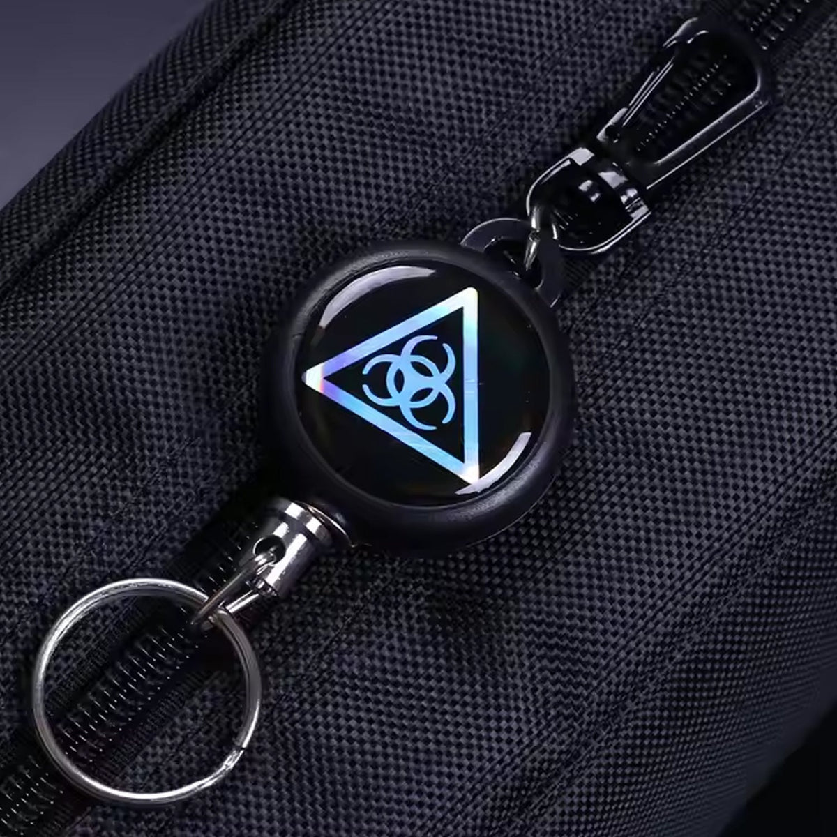 A close-up of a black retractable keychain with a biohazard symbol attached to a dark fabric bag.