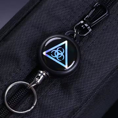 A close-up of a black retractable keychain with a biohazard symbol attached to a dark fabric bag.