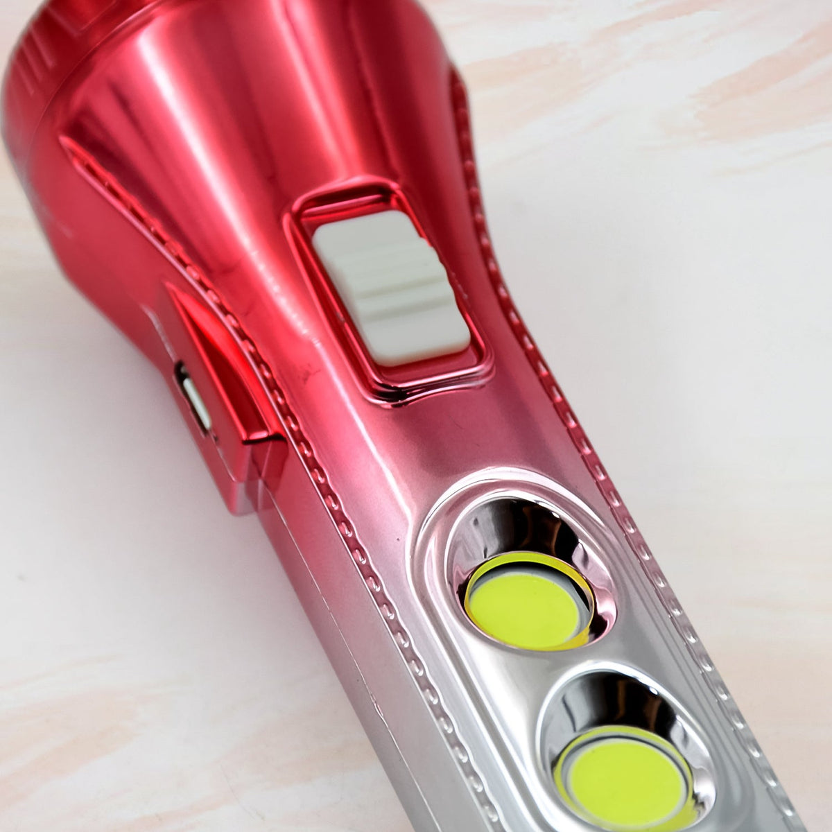 A close-up of the red and silver torchlight's switch and two yellow side lights.