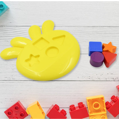 Yellow shape sorter base with separate colorful blocks on a light wooden background, next to red and yellow building bricks.