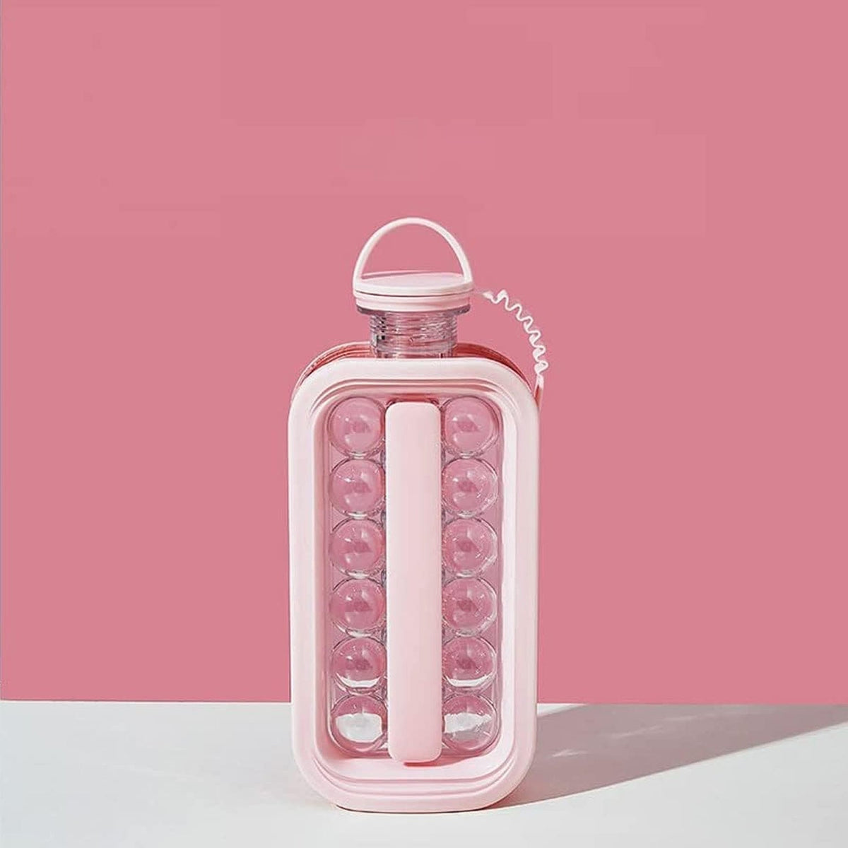 A pink ice ball maker bottle with clear sections containing ice spheres, set against a solid pink background.