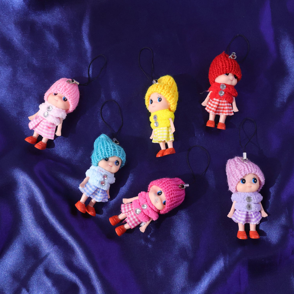Seven colorful doll keychains are scattered across a dark blue satin-like surface.