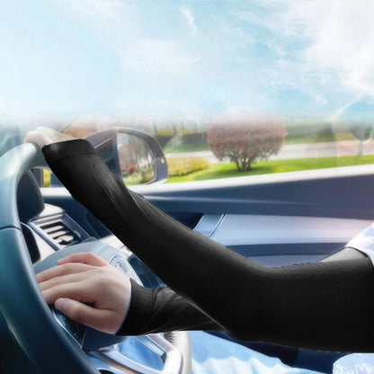 A person driving a car, wearing black compression sleeves on both arms, with a sunny outdoor view.