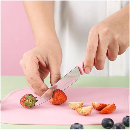 Hands slice a red strawberry on a pink cutting board with a small pink knife, surrounded by other cut fruit.