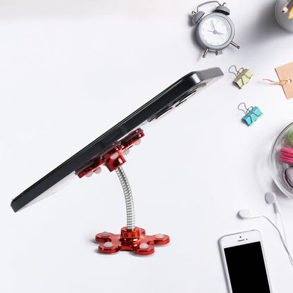 A red flower-shaped phone holder with a flexible silver arm holds a phone on a white desk with office supplies.