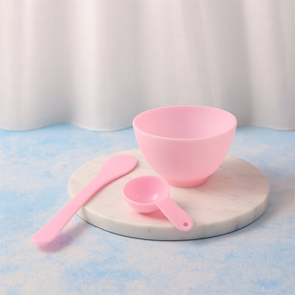 A pink mixing bowl, spatula, and measuring spoon are arranged on a round marble tray against a white curtain.