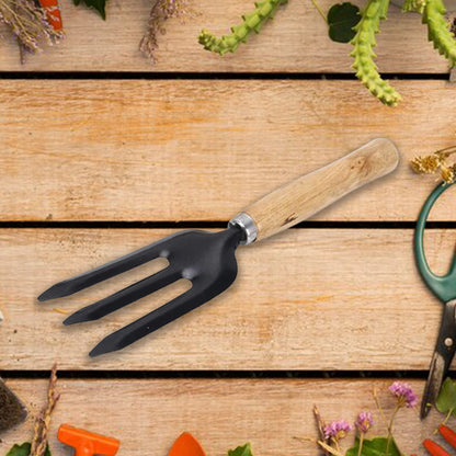 A black three-tine garden fork with a wooden handle is positioned on a rustic wooden surface with various gardening items.
