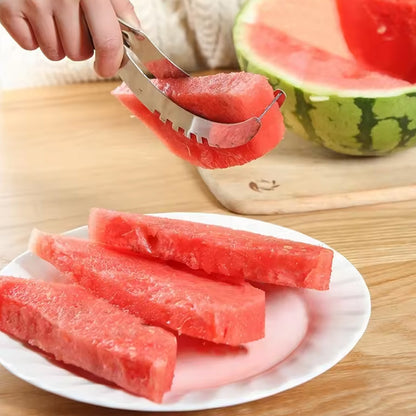 A hand uses a stainless steel watermelon slicer to serve a piece of watermelon onto a white plate with other slices.