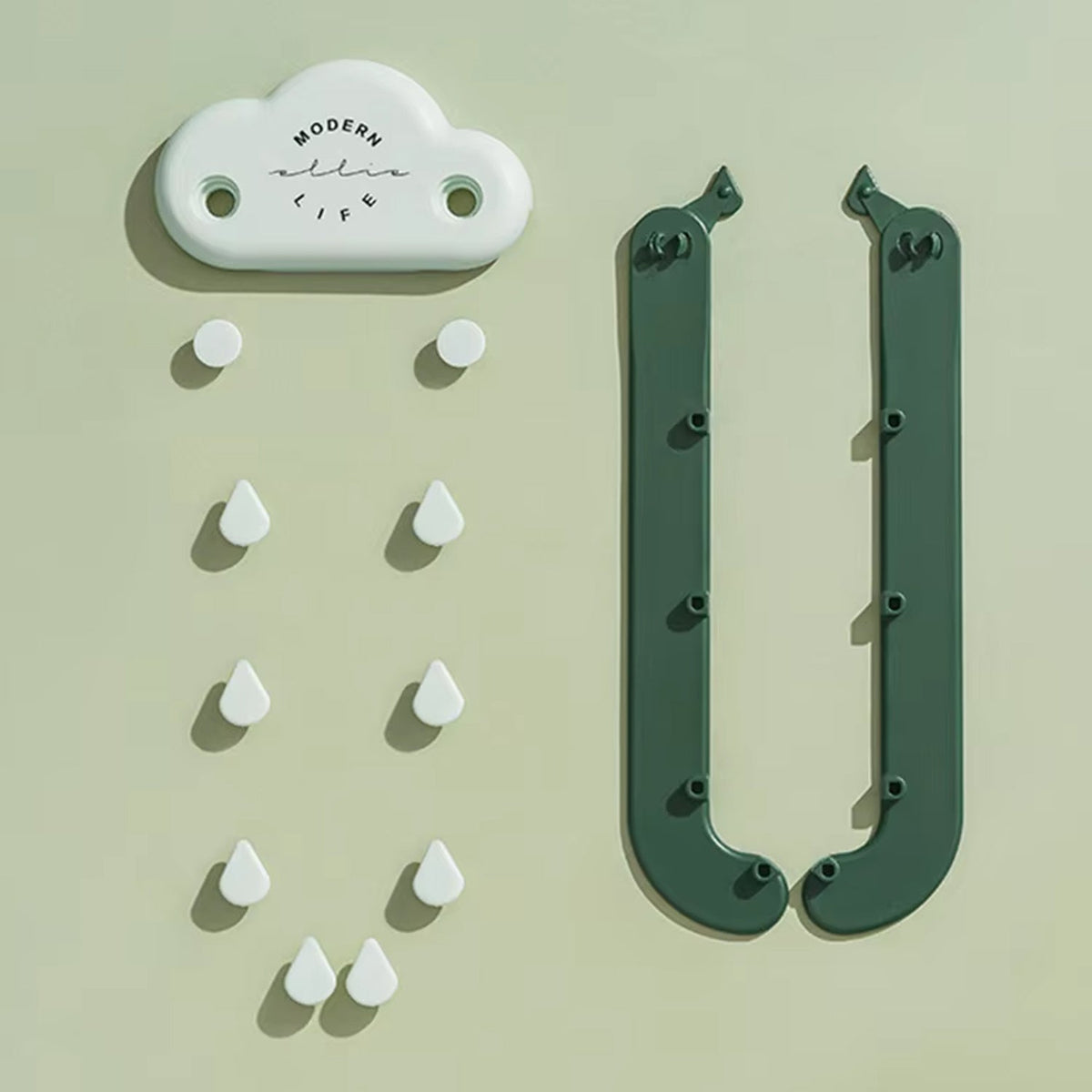 A white cloud-shaped piece and two separate green rain-like arms with white raindrop hooks, laid flat on a light green