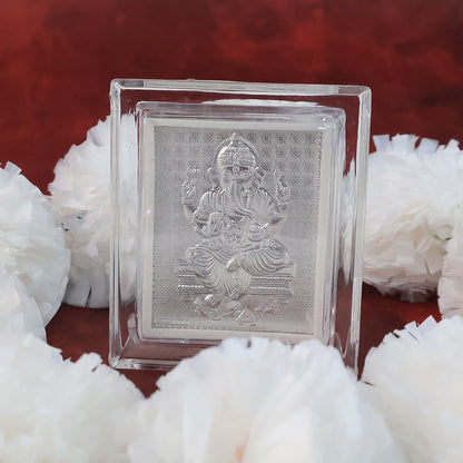 Silver-plated Ganesha idol in an acrylic frame, surrounded by several white fluffy decorations on a red background.