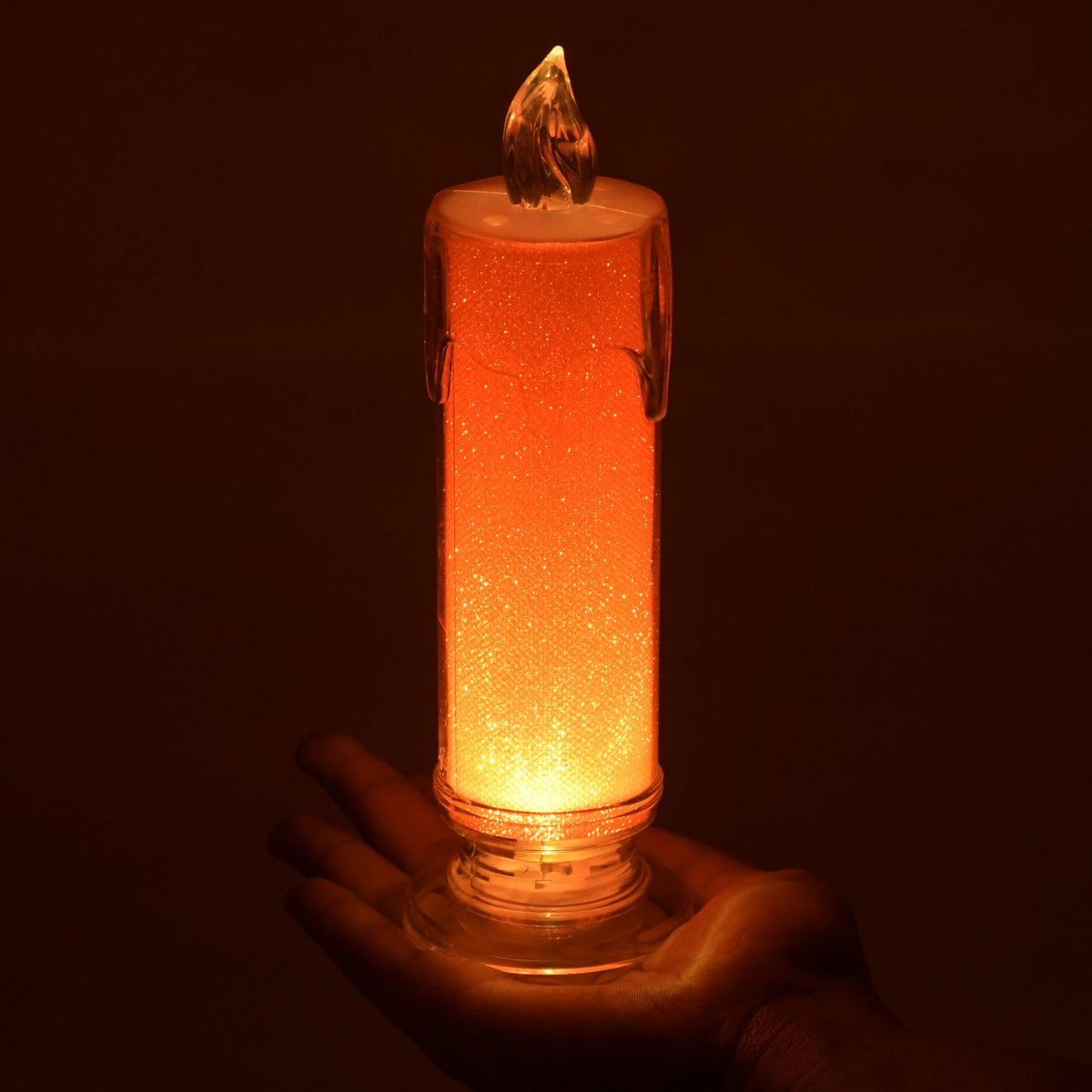 A hand holds the illuminated red LED glitter candle, showcasing its size and warm glow.
