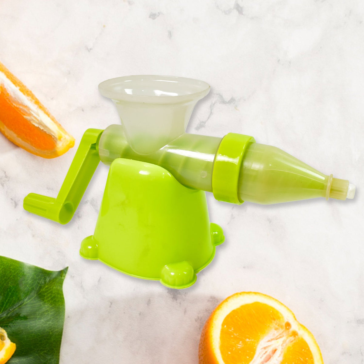 Assembled green manual juicer on a marble surface with orange slices and a green leaf in the foreground.