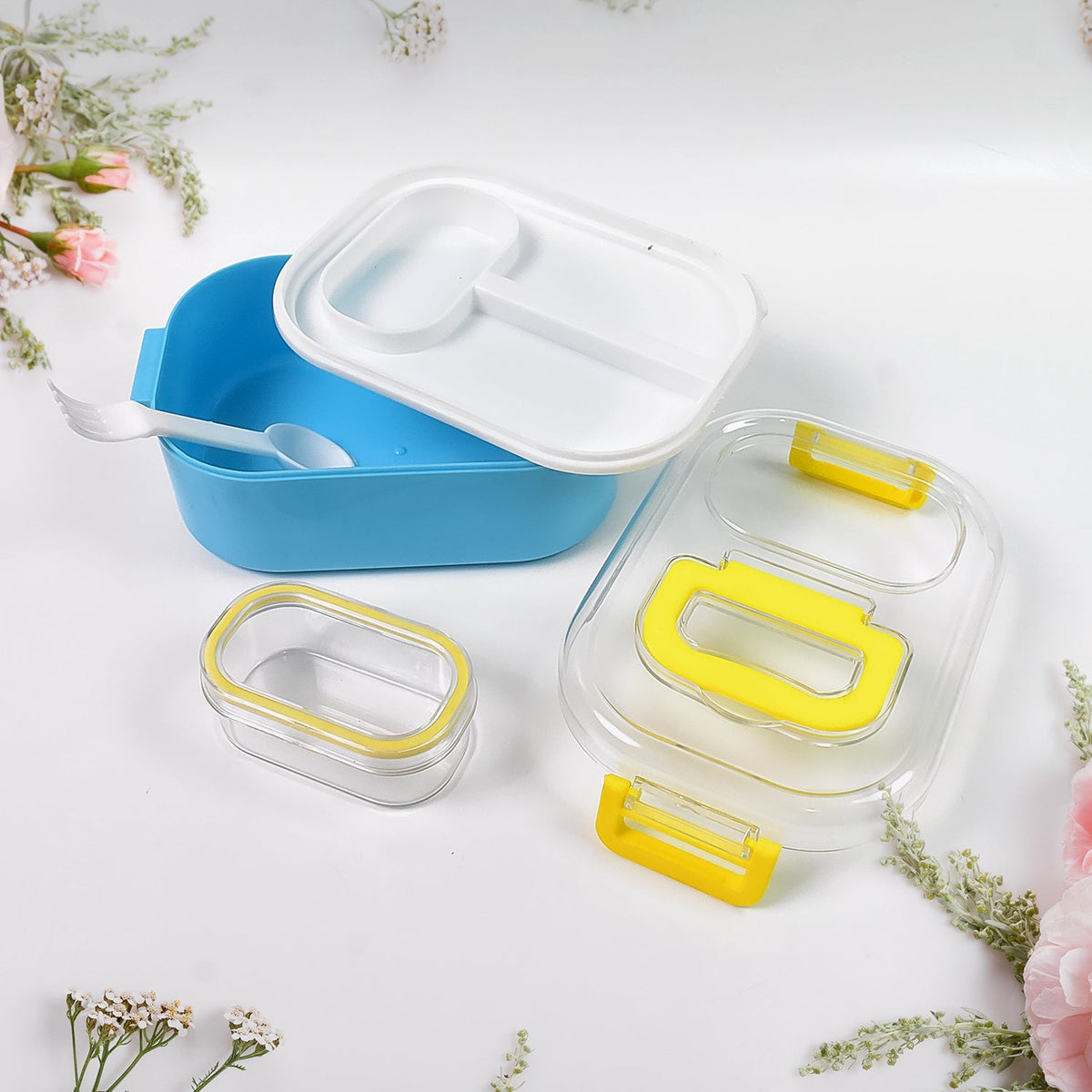 The disassembled blue lunch box, white divider, clear lid, and small container are arranged on a white surface.