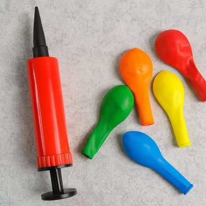 A red and black manual balloon pump next to five uninflated balloons in various colors on a gray background.