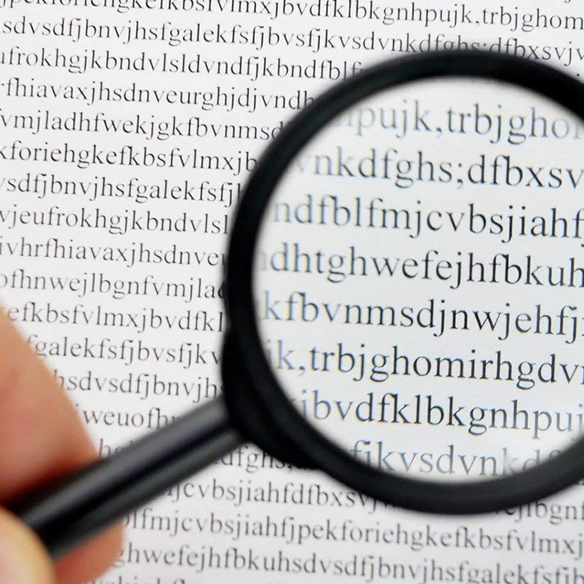 A hand holds a black magnifying glass over a page of text, enlarging the letters for easier reading.