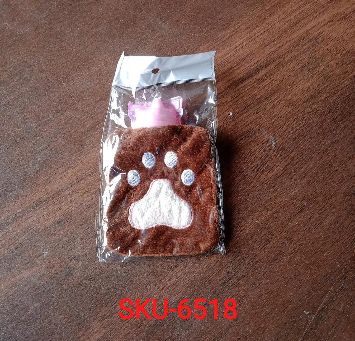 A brown paw print hot water bag is sealed in clear plastic packaging on a wooden surface.