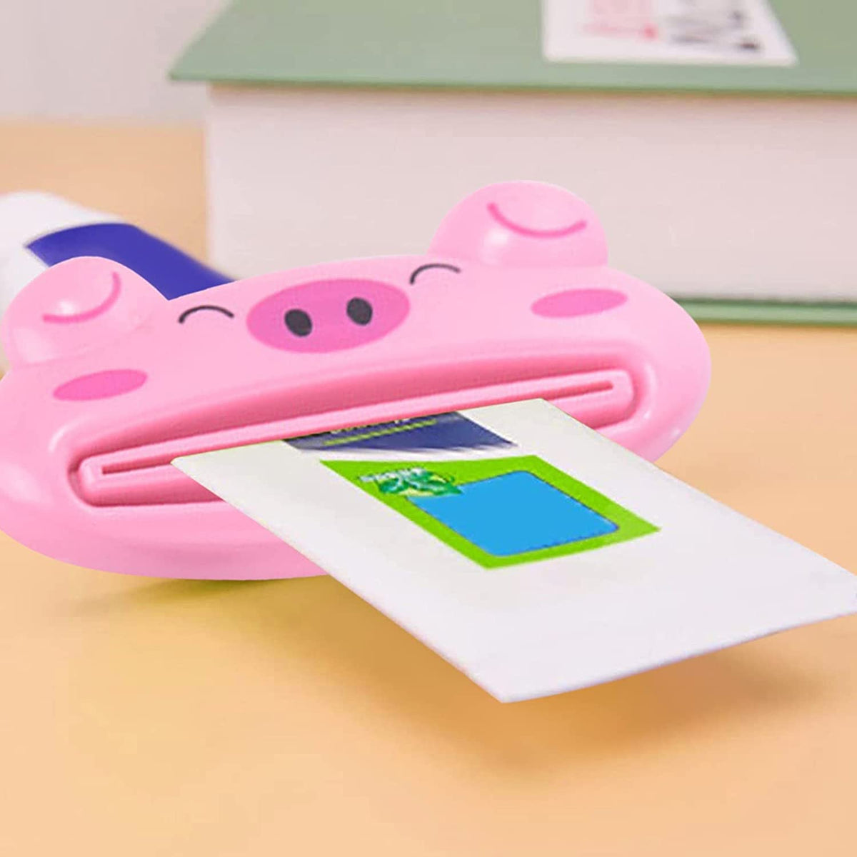 Close-up of a pink pig-shaped toothpaste squeezer with a white and blue toothpaste tube partially inserted on a yellow