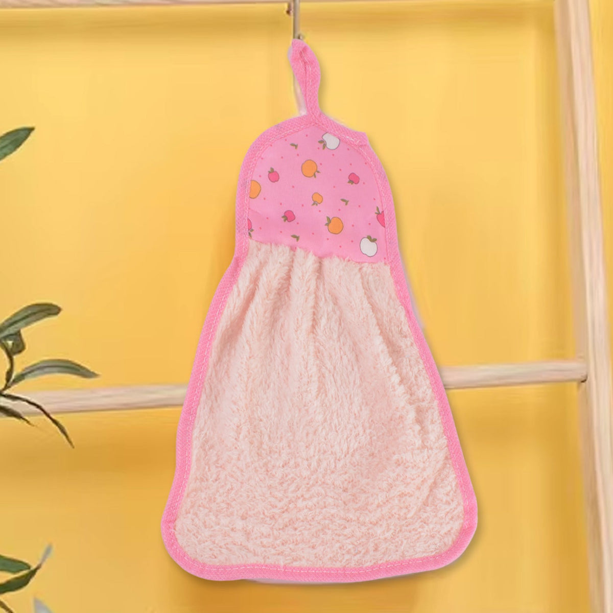 A pink microfiber hand towel with a fruit print top and hanging loop hangs from a hook against a bright yellow wall.