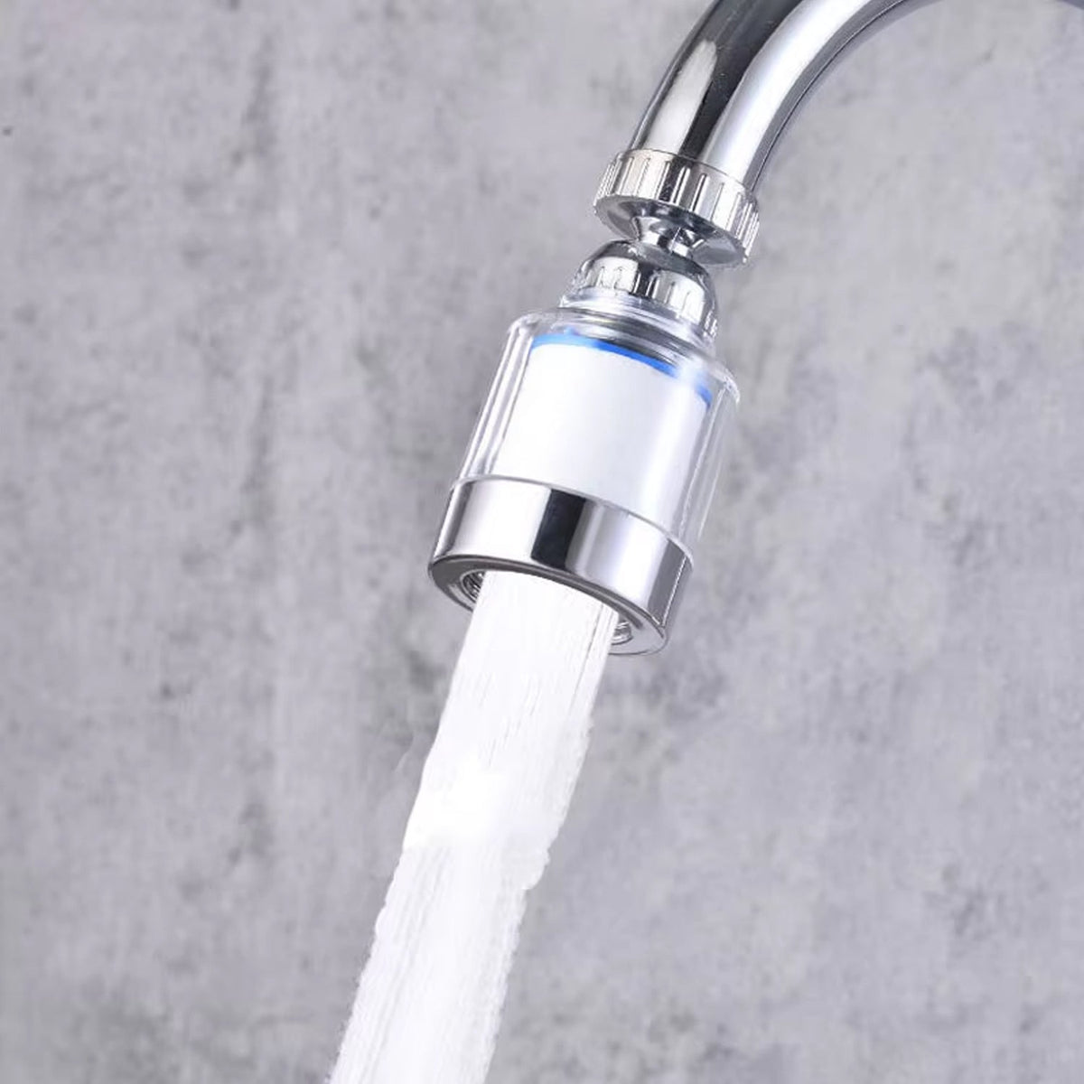 A chrome faucet with the clear plastic aerator attached, spraying a stream of water into a sink with a concrete-like wall.