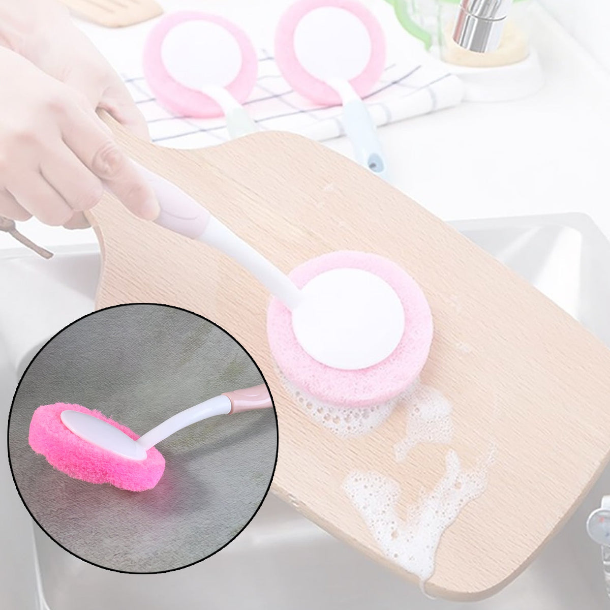 A hand holds a pink and white scrubber, cleaning a wooden cutting board with soap suds in a kitchen sink.