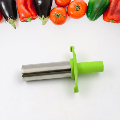 A green and silver chili corer lies horizontally on a white surface, with various vegetables lined up at the top.