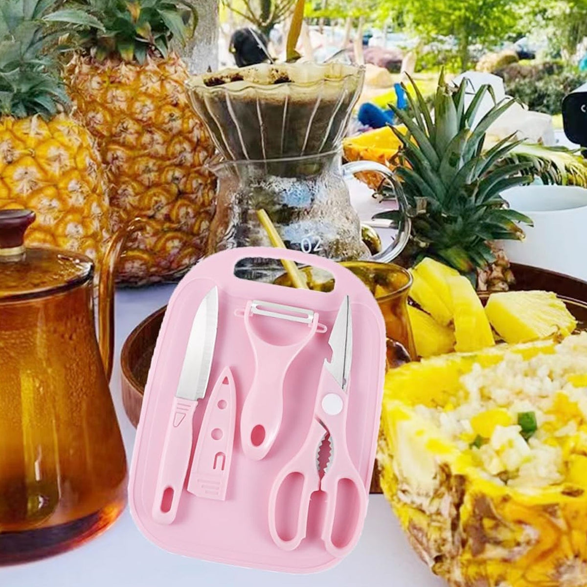 A pink cutting board set is displayed amidst pineapples and a glass coffee maker in an outdoor setting.