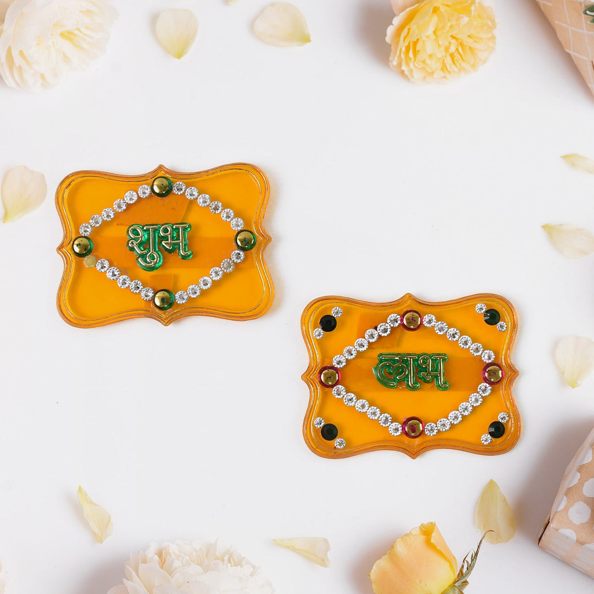 Two yellow Shubh Labh wall hangings with green text and jewels, surrounded by white and yellow flower petals.
