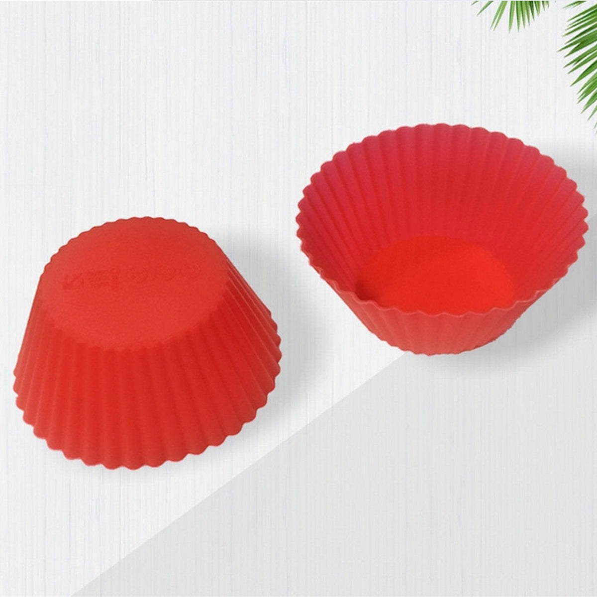 Two red silicone cupcake molds are displayed, one inverted, on a white surface with a plant shadow.