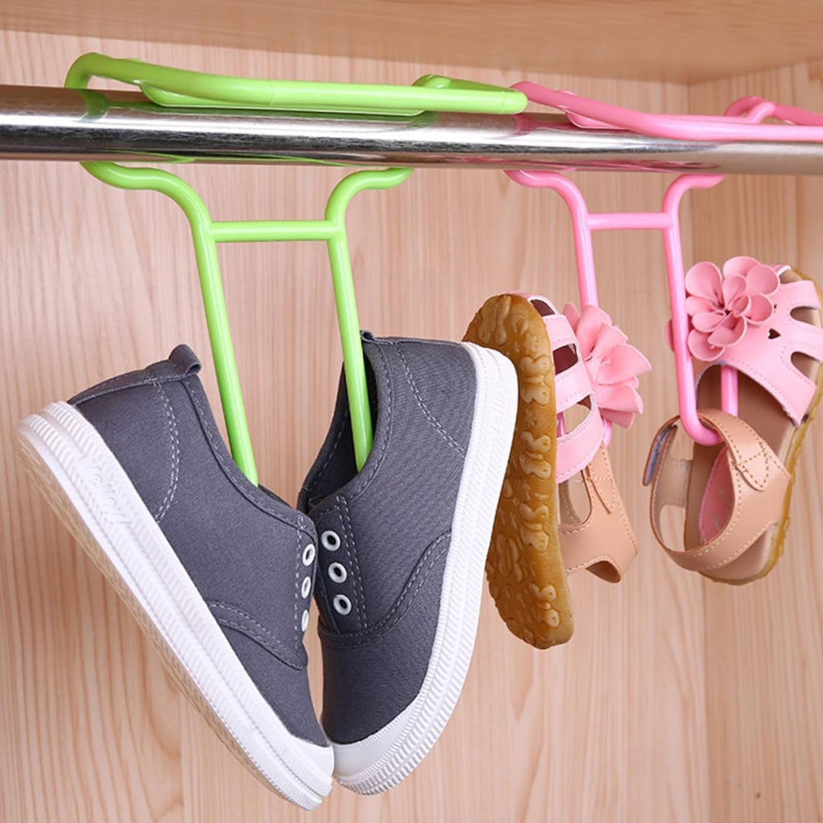 Four plastic shoe hangers, two green and two pink, are holding shoes on a metal rod inside a wooden closet.