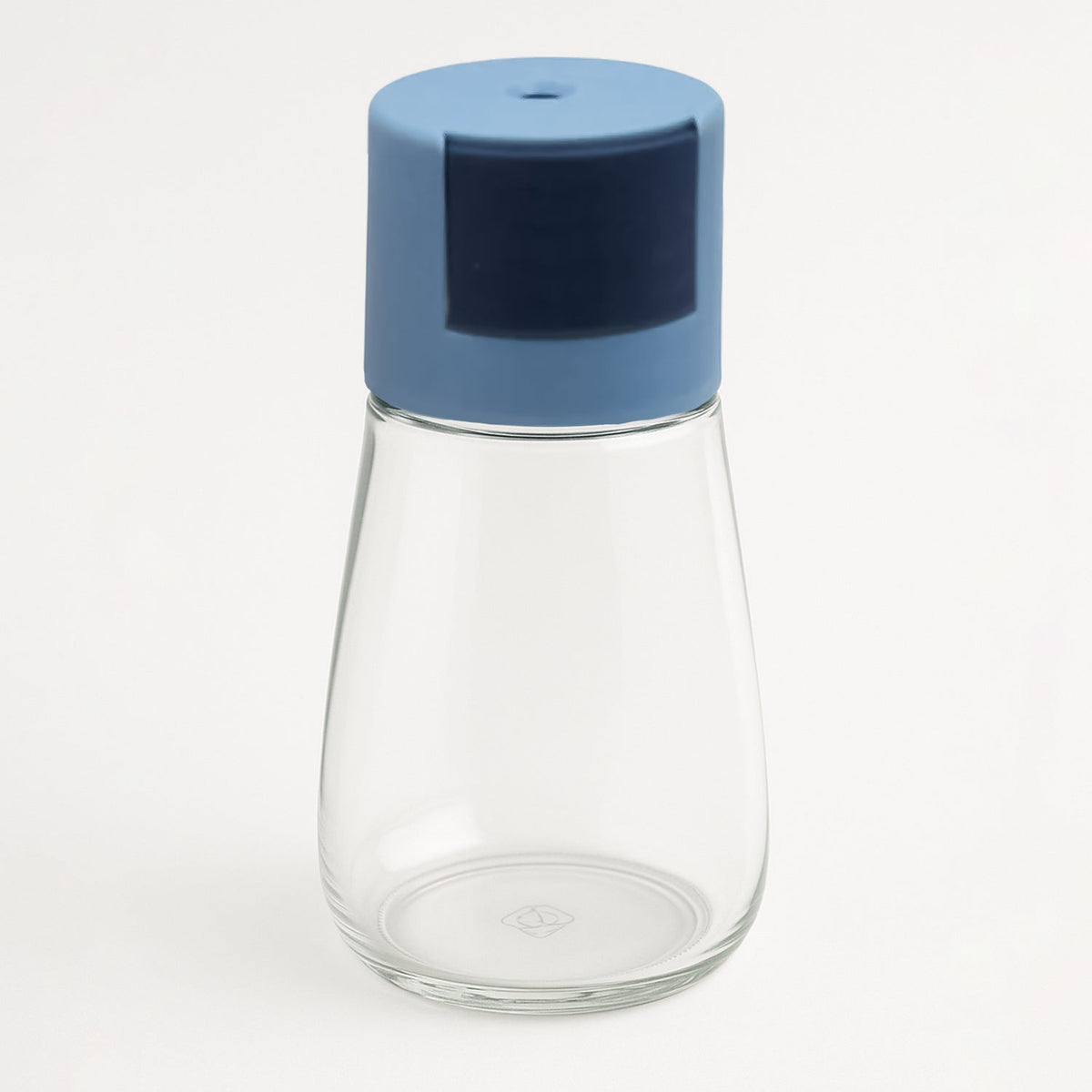 A clear glass spice dispenser with a blue top stands empty on a plain white background.
