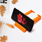 An orange plastic holder on a white desk, holding a black smartphone horizontally, surrounded by autumn leaves.