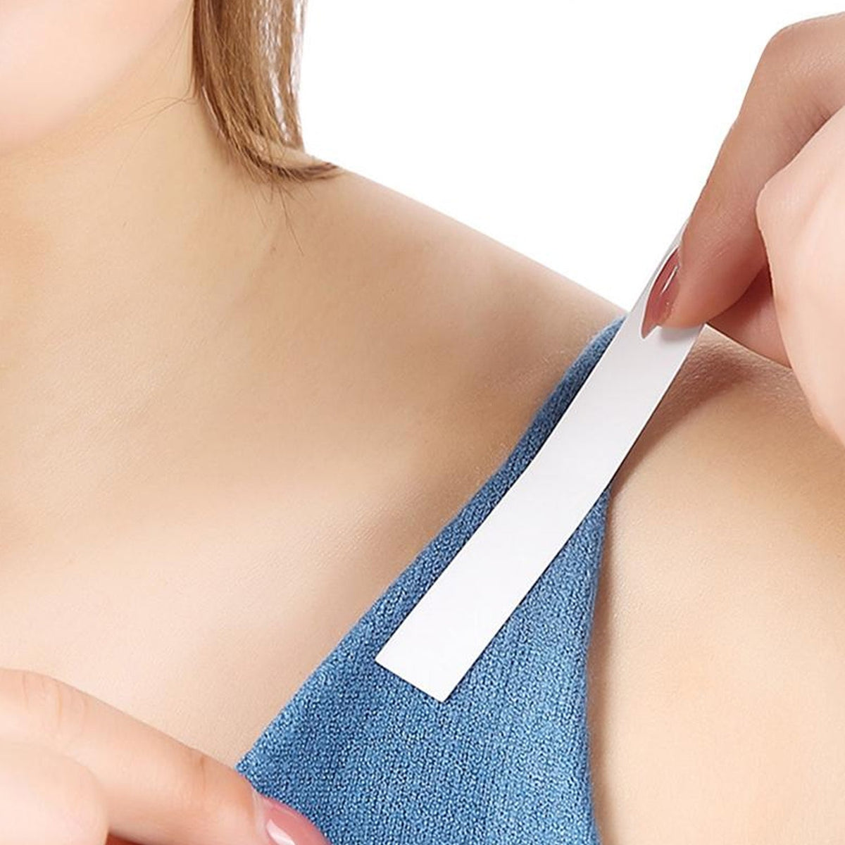 A person adheres a white strip of tape to the blue strap of a garment on their shoulder.