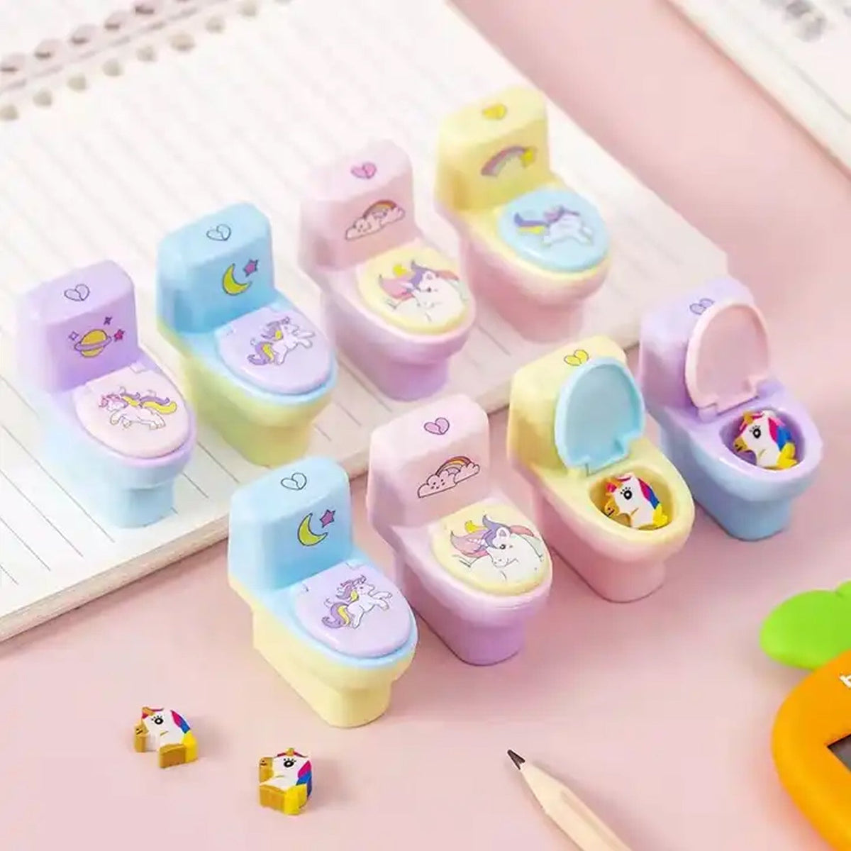 A collection of colorful toilet-shaped pencil sharpeners with unicorn designs, some open with erasers inside, arranged on a