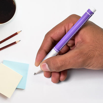 A hand holds a purple gel pen, writing on a white surface next to sticky notes and pencils.