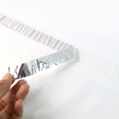 A hand peeling the silver adhesive strip off a clear polybag on a white background.