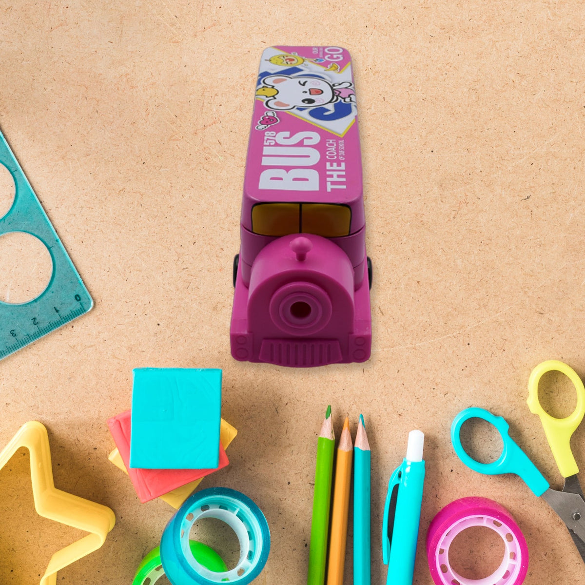 Front view of the pink bus pencil case, revealing a built-in sharpener, surrounded by colorful stationery.