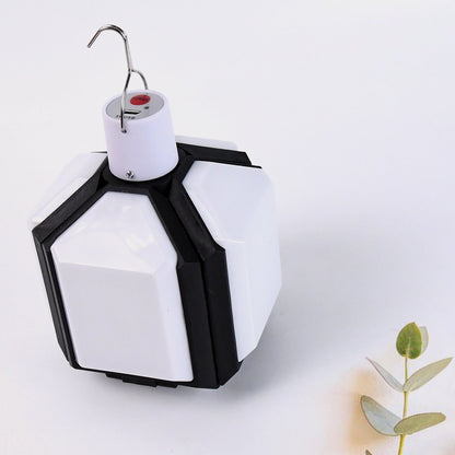 White and black foldable LED lantern in its compact form, with a plant sprig on a white background.