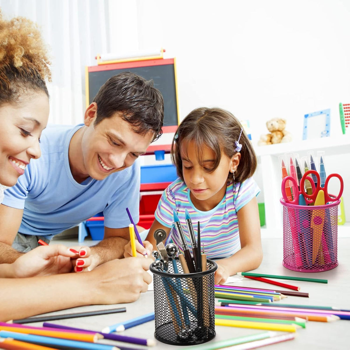 A family draws together with a black mesh pen holder in the foreground and a pink one in the background.