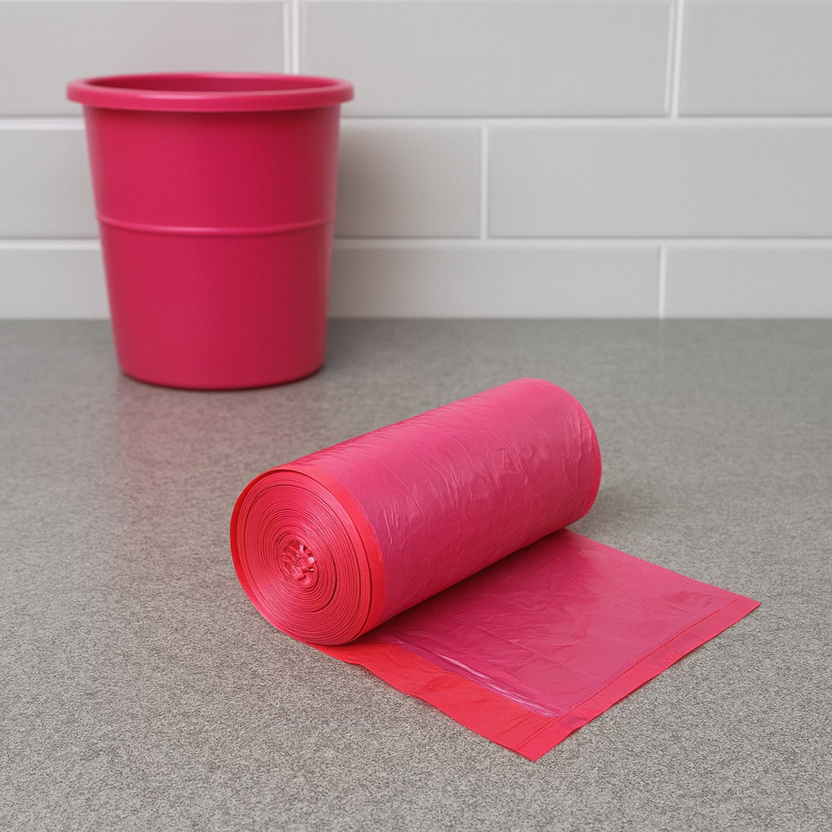 A roll of pink garbage bags sits on a grey counter next to a pink garbage can.